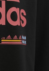 Czarna tkanina z dużym różowym logo "adidas", z mniejszymi, kolorowymi logo i graficznymi detalami na dole.