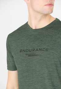Tummanvihreä lyhythihainen t-paita, joka on valmistettu teksturoidusta kankaasta. Keskellä musta "ENDURANCE" -logo. Pyöreä pääntie, rento malli.