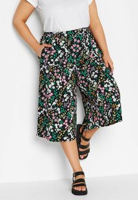 Svarta blommiga culottes med färgglada blommor och gröna accenter. Har ett elastiskt midjeband och sidofickor. Kombineras med svarta sandaletter.