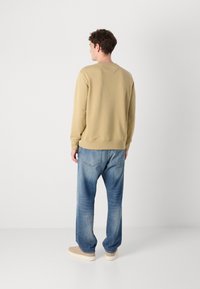 Khaki sweatshirt met ribbelmanchetten en -zoom, gecombineerd met lichtblauwe jeans met een relaxte pasvorm en zichtbare achterzakken. Bruine schoenen maken de look compleet.