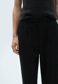 Black tailored trousers with a straight fit, featuring front pleats and a smooth texture. Worn with a gray sleeveless knit top.