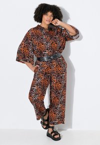 Twee-delige set met een oranje en zwarte luipaardprint. De top heeft een losse pasvorm met een kraag en zwarte wijde broekspijpen. Gecorrigeerd met zwarte sandalen.