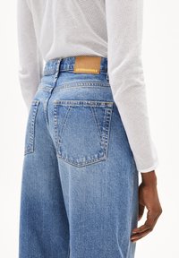 Jean en denim bleu clair avec une finition légèrement délavée. Présente une patch en cuir étiqueté "ARMEDANGELS" à la taille arrière et deux poches arrière.