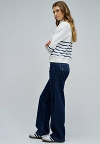 Sudadera blanca y navy a rayas combinada con jeans de pierna ancha de color azul oscuro y zapatillas blancas/negras. Tejido suave con un corte relajado.