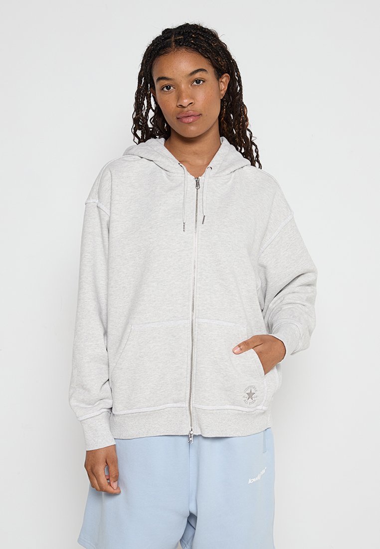 Hellegraue Kapuzenjacke mit Reißverschluss aus weichem, strukturiertem Stoff. Sie verfügt über eine Fronttasche und eine verstellbare Kapuze mit Kordelzug. Auf der Tasche befindet sich ein Logo-Detail.