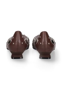 Chaussures en cuir marron avec un bout arrondi, dotées d'accents circulaires métalliques et d'un petit talon. L'arrière est orné de rivets décoratifs.