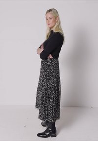 Schwarzes Langarmoberteil mit einem gemusterten schwarz-weißen Rock mit fließender Textur. Kombiniert mit glänzenden schwarzen ankle boots.