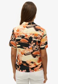 Camisa de manga corta con un vibrante estampado floral en colores naranja, rosa y negro; tela lisa con cuello con solapa y detalles de botones.