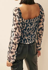 Blouse met pofmouwen in een abstract patroon van blauw en crème; gerimpelde achterkant; gedragen met glanzende zwarte leren broeken met witte stiksels.