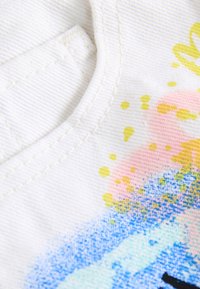 White fabric with a textured finish featuring colorful abstract patterns in pink, yellow, and blue. Stitching detail around the neckline.