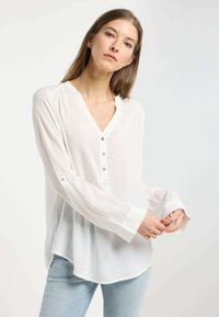 Blusa bianca a maniche lunghe con scollatura a V, dotata di un bottone e dettagli sui polsini, realizzata in tessuto leggero; texture liscia e vestibilità morbida.