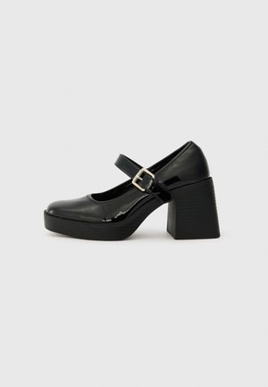 Black patent leather Mary Jane heels with a round toe, wide block heel, adjustable buckle strap, and textured sole.