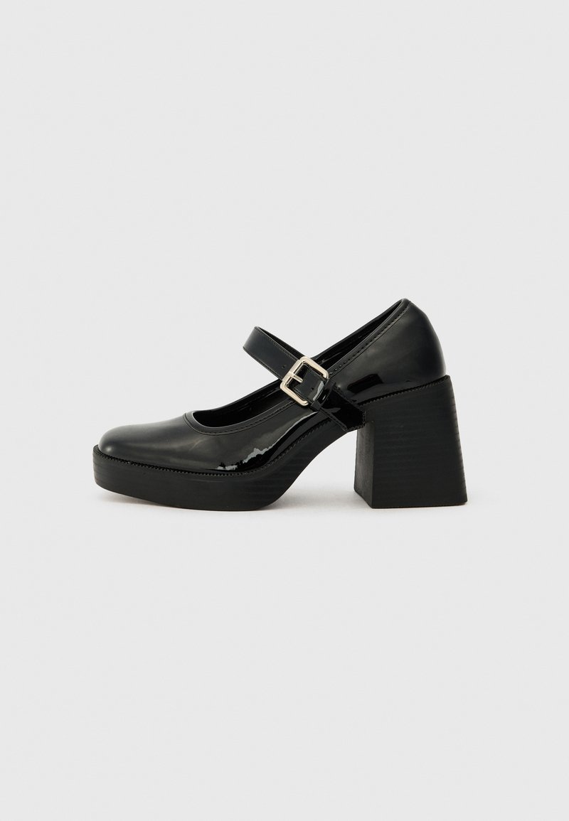 Black patent leather Mary Jane heels with a round toe, wide block heel, adjustable buckle strap, and textured sole.