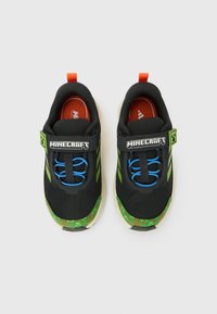 Mustad Minecrafti-teemalised tossud rohelise pikslilise mustriga, siniste elastsete paelte ja oranžide tõmbenuppudega, vaadatuna ülevalt valgel taustal.