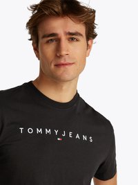 T-shirt en coton noir avec le texte "TOMMY JEANS" brodé en lettres blanches et un petit accent de logo coloré. Encolure ronde.