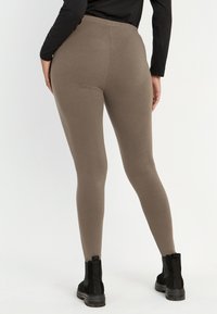 Leggings in een zachte, taupe stof met een gladde textuur. Hoge tailleband en een aansluitend ontwerp, gecombineerd met zwarte enkellaarsjes.