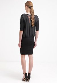 Schwarzes Kleid mit einem eng anliegenden unteren Teil und einem lockeren Oberteil mit einem Spitzenrücken. Kurze Ärmel und ein Reißverschlussverschluss auf der Rückseite.