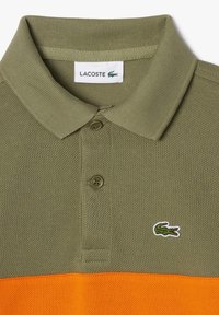 Olivengrøn polo shirt med ribbet krave og tre knapper; har en orange vandret stribe og hvidt krokodillelogo på venstre bryst.