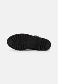 Suela de zapato de goma negra con un patrón de relieve texturizado. Presenta un logotipo prominente y múltiples líneas de agarre para tracción y durabilidad.