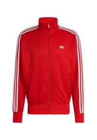 Červená sieťovaná bunda na zips s vysokým golierom, bielymi tromi pruhmi pozdĺž rukávov a logom na ľavej strane hrude. Lemované manžety a spodný okraj.