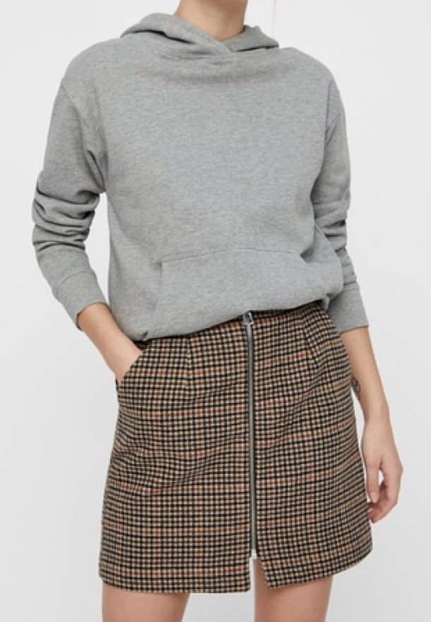 Sudadera gris con capucha y un bolsillo frontal, combinada con una falda corta de cuadros marrones con cremallera al frente que presenta patrones de cuadros negros y marrones.
