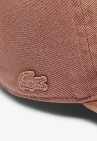 Gorra de suave tela rosa, con una superficie texturizada y un logo bordado en hilo a juego. Visera curvada con costuras visibles.