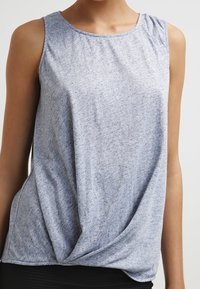 Světle modrý top bez rukávů vyrobený z měkké, strukturované látky. Má kulatý výstřih a detail zkrouceného uzlu v přední části.