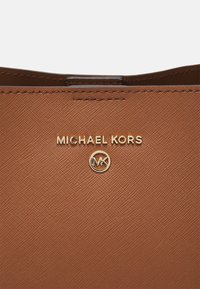 Tan gekorreld leren handtas met goudkleurige, reliëf ''MICHAEL KORS'' logo en ronde MK-embleem. Heeft strakke lijnen en een minimalistisch ontwerp.