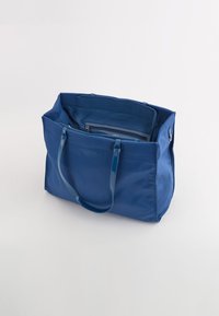 Blauwe nylon draagtas met glanzende handvatten, open bovenkant en binnenzak met ritssluiting. Heeft een brede rechthoekige vorm en een gladde textuur.