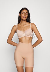 Nøgen bh med blondedetaljer og formede skåle, parret med højttalende shaping shorts. Begge beklædningsgenstande har en glat overflade og sømløst design.