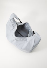 Svijetlosiva torba od mekog materijala s patentnim zatvaračem i crnim ručkama. Unutrašnjost je obložena glatkim materijalom i prostornog je dizajna.