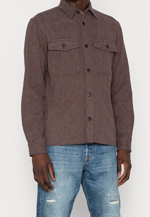 Braune Wollmischung Hemdjacke mit zwei Fronttaschen; verfügt über schwarze Knöpfe, einen klassischen Kragen und eine lässige Passform. Über Jeans getragen.