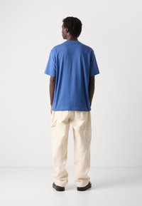 Zila kokvilnas T-kreklu ar īsām piedurknēm, jaunā aplis dekoltē un brīvā griezumā, savienots ar krēmbaltām biksēm un melnā krāsā kedām.