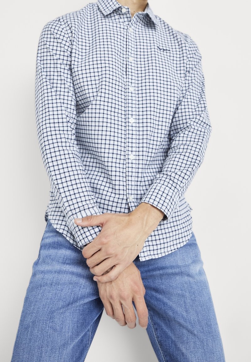 Blauw-wit geruit overhemd met knoopsluiting en lange mouwen, gemaakt van geweven stof, gedragen met lichtblauwe spijkerbroek.