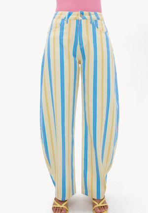 Pantalon taille haute à jambes larges avec des rayures verticales jaunes, bleues et blanches, porté avec des sandales jaunes et un haut rose.