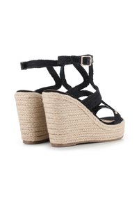 Sandalias de cuña negras con tiras trenzadas y un tacón cubierto de yute. Presenta un hebilla ajustable en el tobillo y un diseño de punta abierta, con una superficie texturizada.