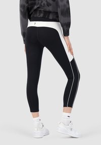 Svartvita idrottstights har en strömlinjeformad design med sidostenar och hög midja. Elastiskt tyg och cropped längd.