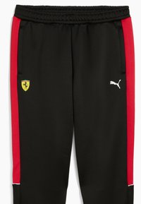 Sorte atletiske bukser med røde sidelister, elastisk talje, med et gult Ferrari-logo og hvidt Puma-logo på venstre ben.