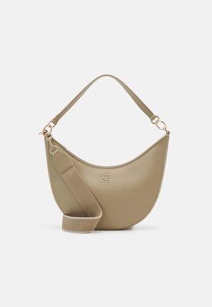 Sac à main beige en forme de croissant avec une poignée courte, une large bandoulière en tissu amovible et un petit emblème doré sur le devant sur fond blanc.