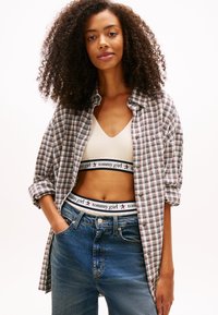 Camicia oversize a quadri grigia, blu e bianca, indossata sopra un top corto beige con fascia logo. Jeans blu a vita alta con tasche.