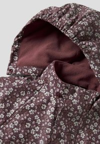 Saka s květinovým vzorem s fialovým povrchem, vybavené měkkou bordó fleecovou podšívkou. Obsahuje kapuci a patentní knoflíky.