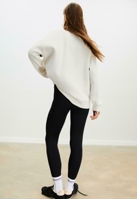 Overmaat witte sweatshirt, zwarte leggings en zwarte sneakers. Het sweatshirt heeft wijde mouwen en een ronde zoom. Eenvoudig, zonder patronen.