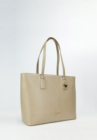 Beżowa torebka tote z ekoskóry z dwoma uchwytami, błyszczącym złotym akcentem i detalem z logo. Prostokątny kształt o gładkiej fakturze.