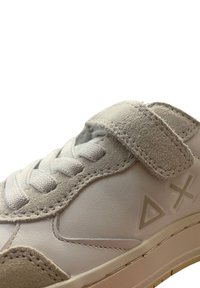 Sneaker bianco con una cintura in suede grigia testurizzata, lacci flat e sottili accenti geometrici sul lato. Design elegante e minimalista.