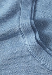 Tissu tricoté bleu clair avec une texture lisse. Présente un col arrondi et des détails fins en côtes le long des bords.