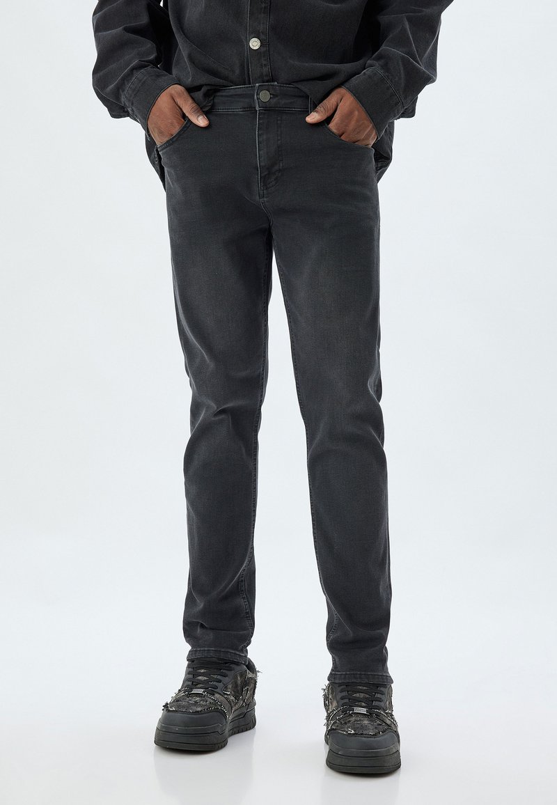 Jeans in denim grigio scuro con vestibilità slim, dotati di tasche frontali e chiusura con bottone in vita, abbinati a sneakers nere con trama.