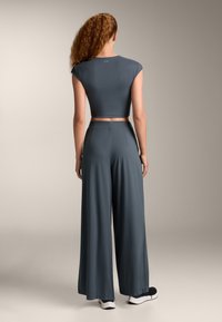 Gray two-piece outfit featuring a cropped top with cap sleeves and wide-leg pants. Fabric appears smooth, with a tailored fit and minimal design.