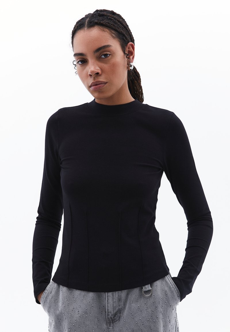 Maglietta nera a maniche lunghe con collo alto, design aderente, texture liscia e dettagli delle cuciture sottili, abbinata a pantaloni grigi chiari con motivo.
