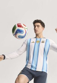 Bijela majica s svijetloplavim vertikalnim prugama i crnim ovratnikom, sa FIFA simbolom i tri zvjezdice. Tamnoplave kratke hlače s svijetloplavim naglascima. Lopta za nogomet iznad.