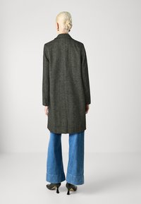 Cappotto grigio intrecciato con design su misura, maniche lunghe e apertura posteriore. Abbinato a pantaloni jeans svasati e scarpe con tacco nere.